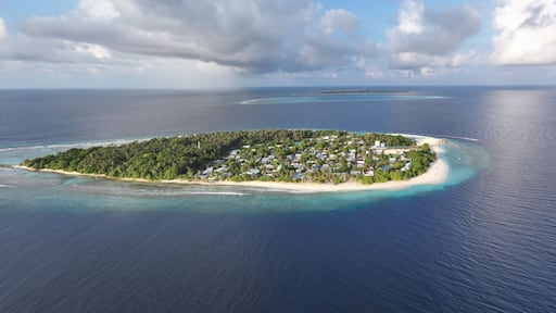 Aerial view of an island lush with green vegetation, white sandy beaches, and clusters of buildings surrounded by the deep blue sea, Maalhos, Baa Atoll, Maldives.