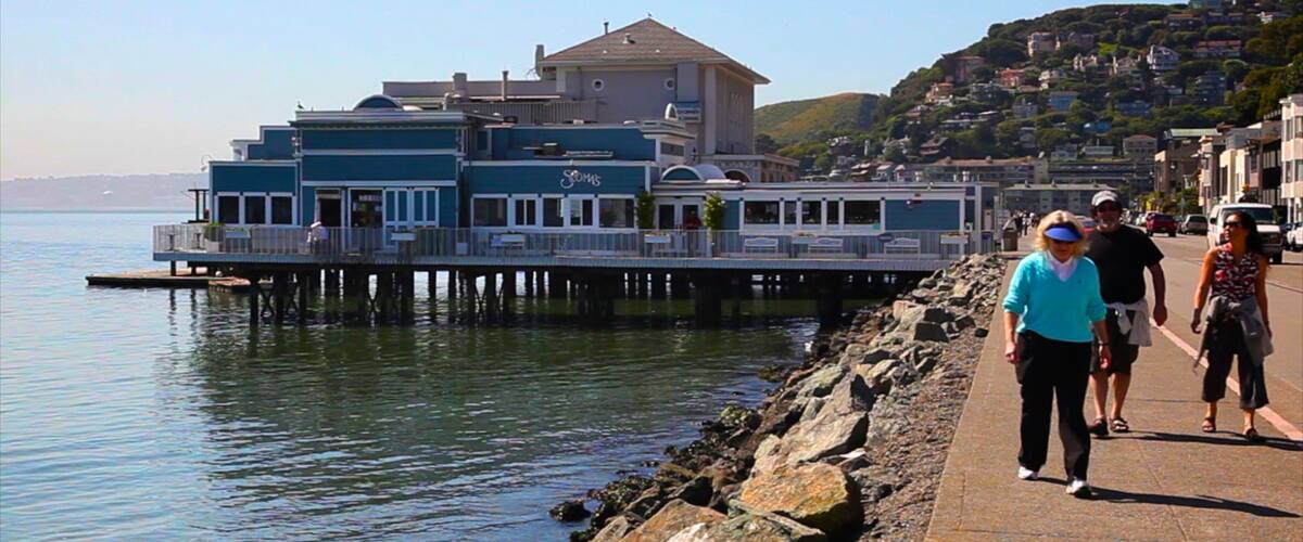 A waterfront pier with a restaurant and a building with a tower.