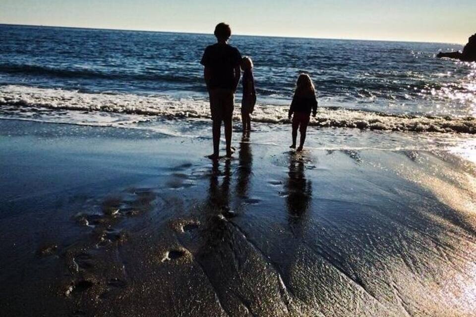 En strand med våt sand och fotspår, en person som står där, och havet i bakgrunden.