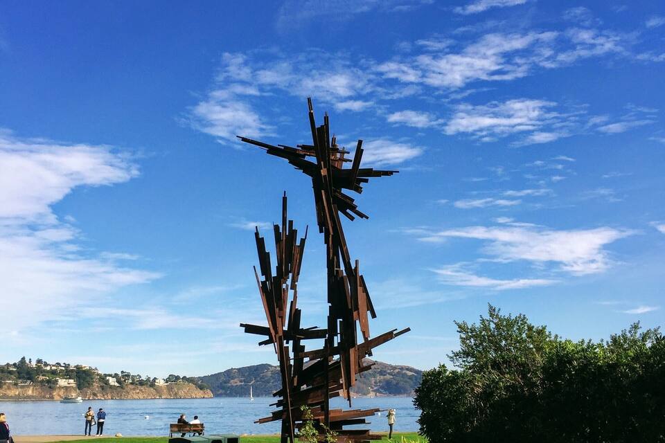 A sculpture in a park with a lake and mountains in the background.