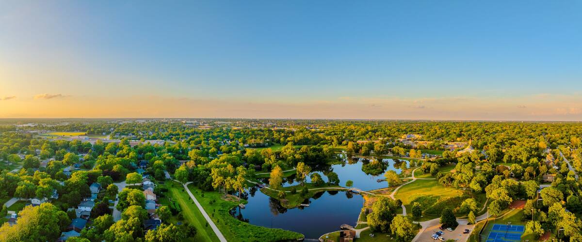 Un parque grande con un lago, rodeado de zonas residenciales y un horizonte urbano distante.