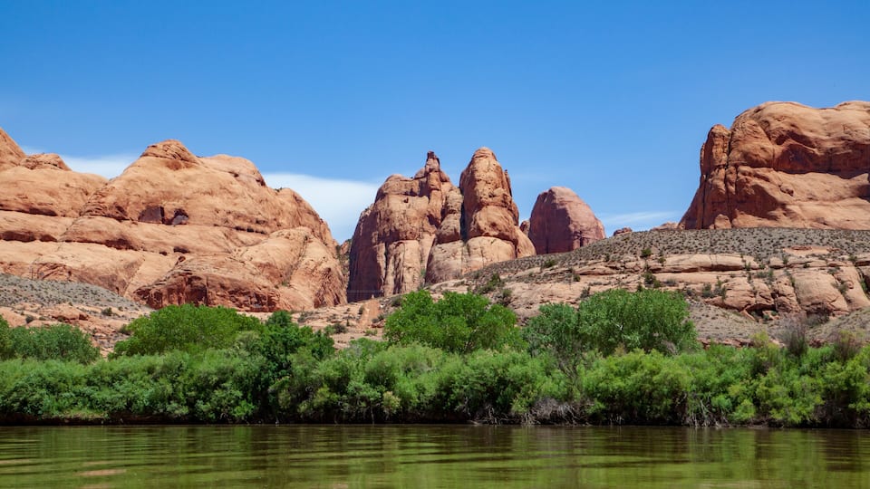 A river with red rock formations and green vegetation.