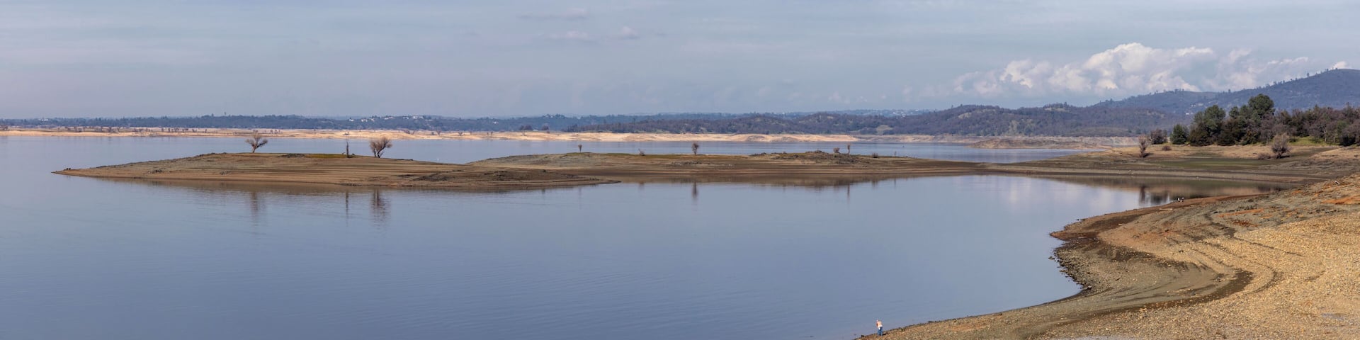 A calm lake with sandy shores and distant mountains.