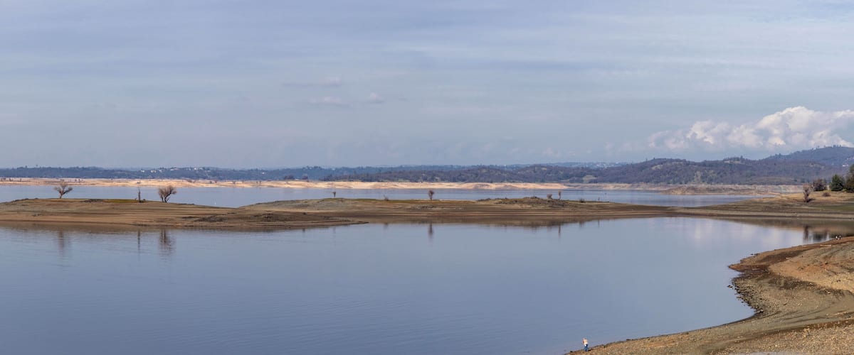 A calm lake with sandy shores and distant mountains.