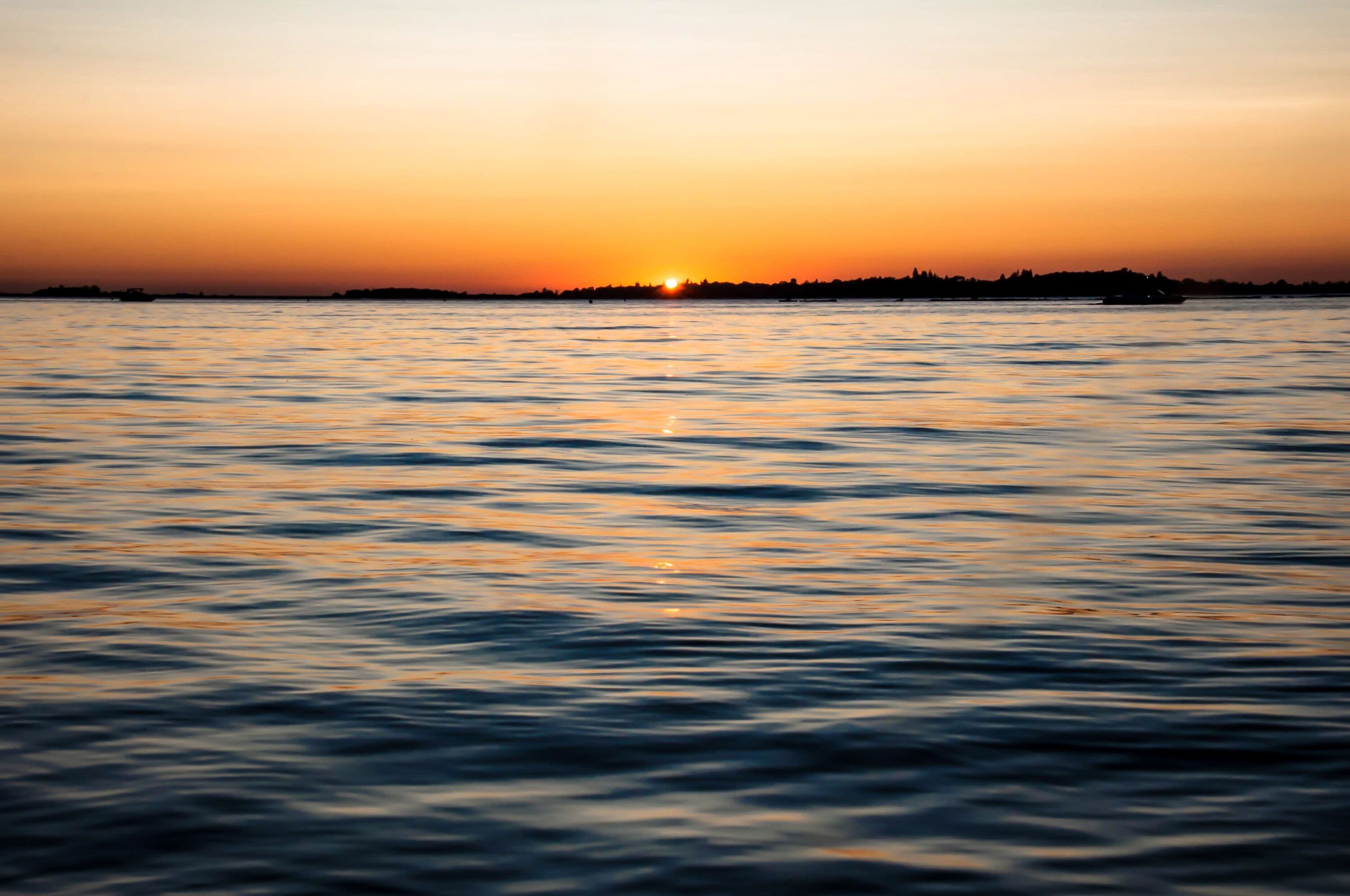Un atardecer sobre un mar tranquilo, con la silueta de una costa lejana.