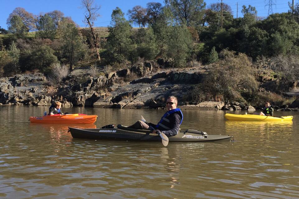 Three kayaks on a calm river surrounded by trees and rocky terrain.