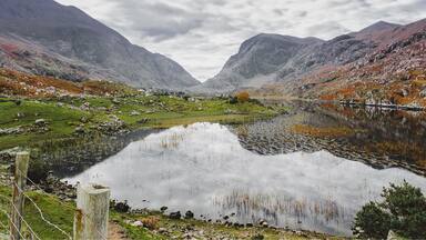 A mountainous landscape with a lake reflecting the sky, surrounded by rocky terrain and sparse vegetation.