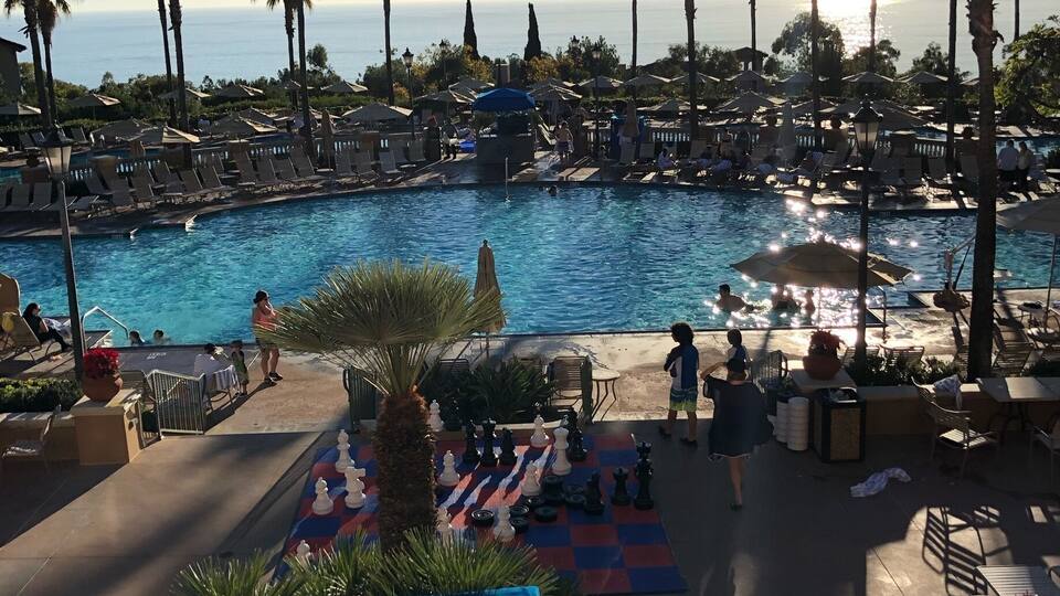 Ein Poolbereich mit Liegestühlen, einem Schachbrett und Palmen.