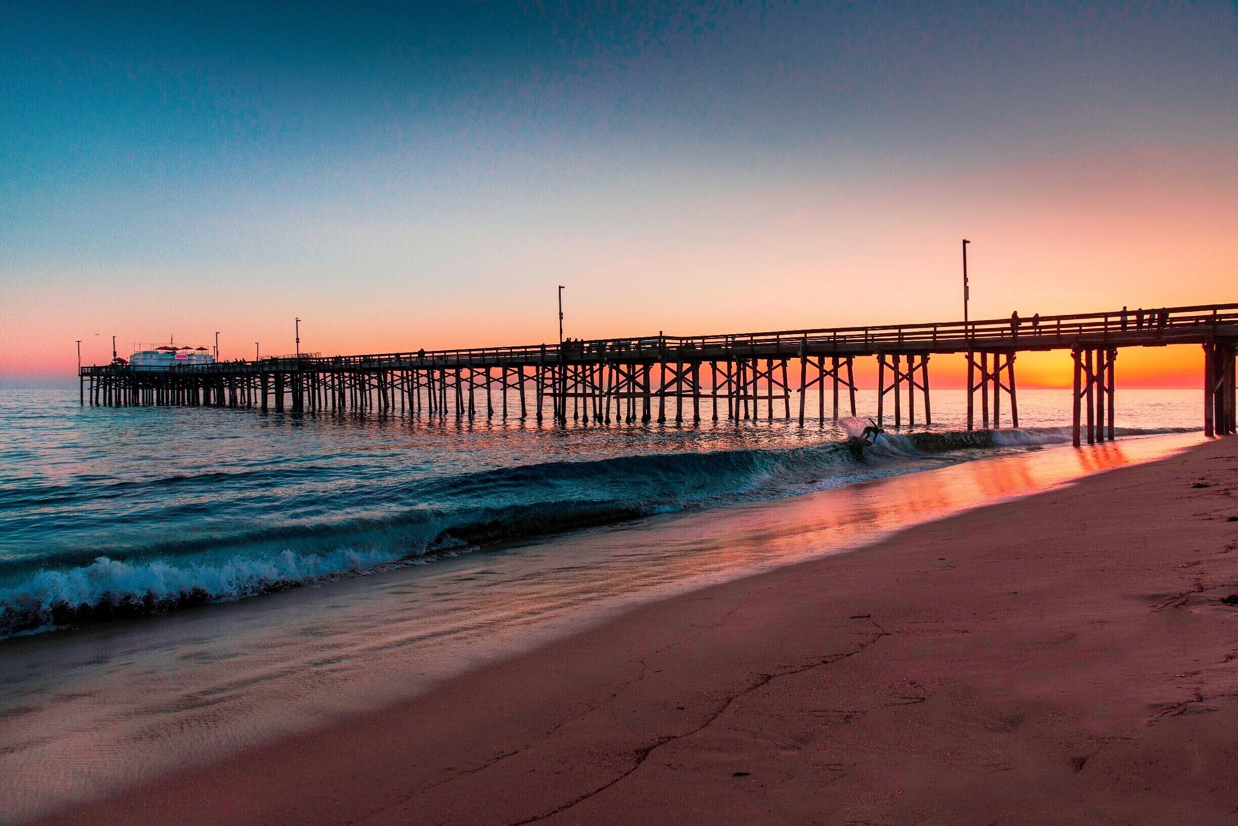A skim boarder gets in a final wave of the day kicking up a twilight splash of gold under the shadow of the Balboa Pier in Newport Beach.