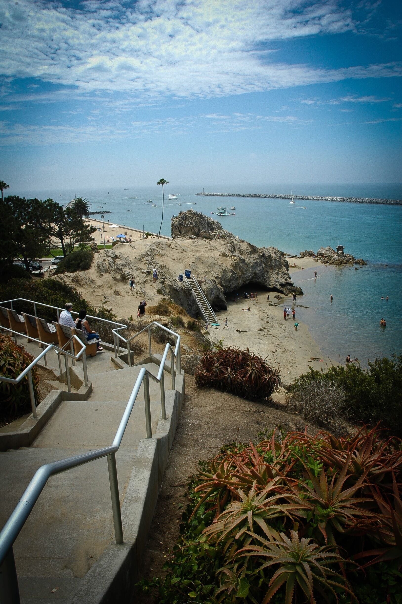 Une plage côtière avec un escalier descendant vers le rivage, entourée d’un terrain rocheux et d’une végétation clairsemée.
