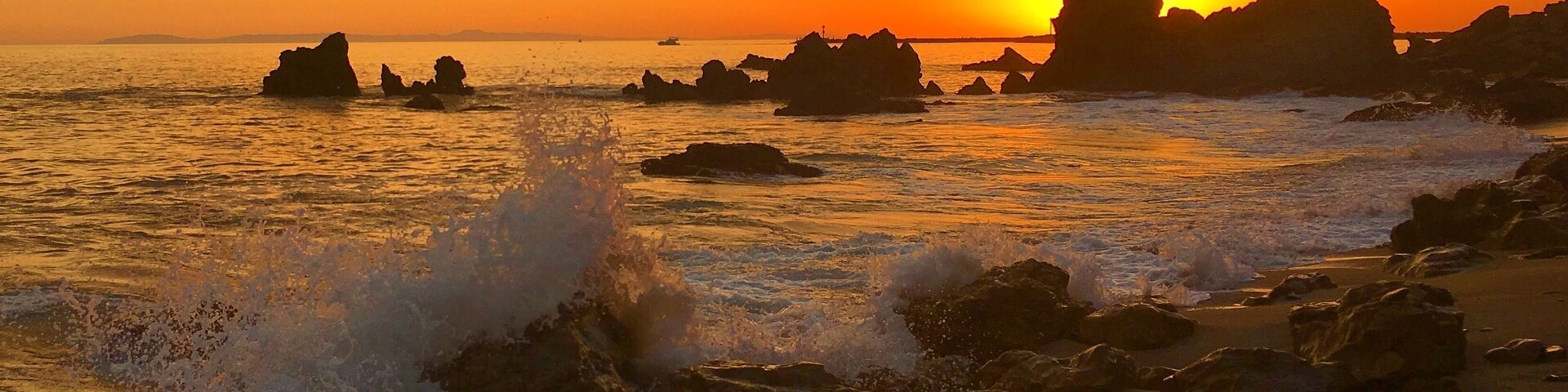 Um pôr do sol sobre um litoral rochoso com ondas quebrando na praia.