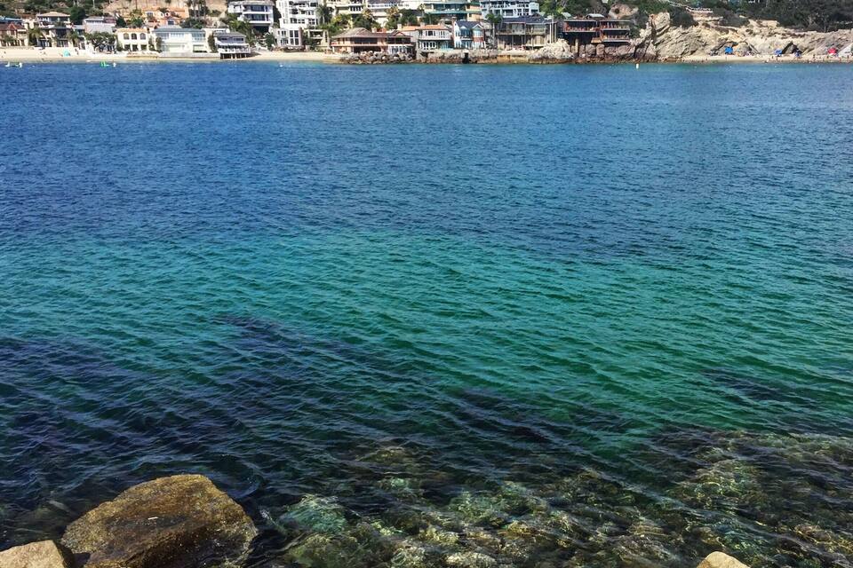 A coastal town with clear blue waters, rocky shore, and residential buildings.