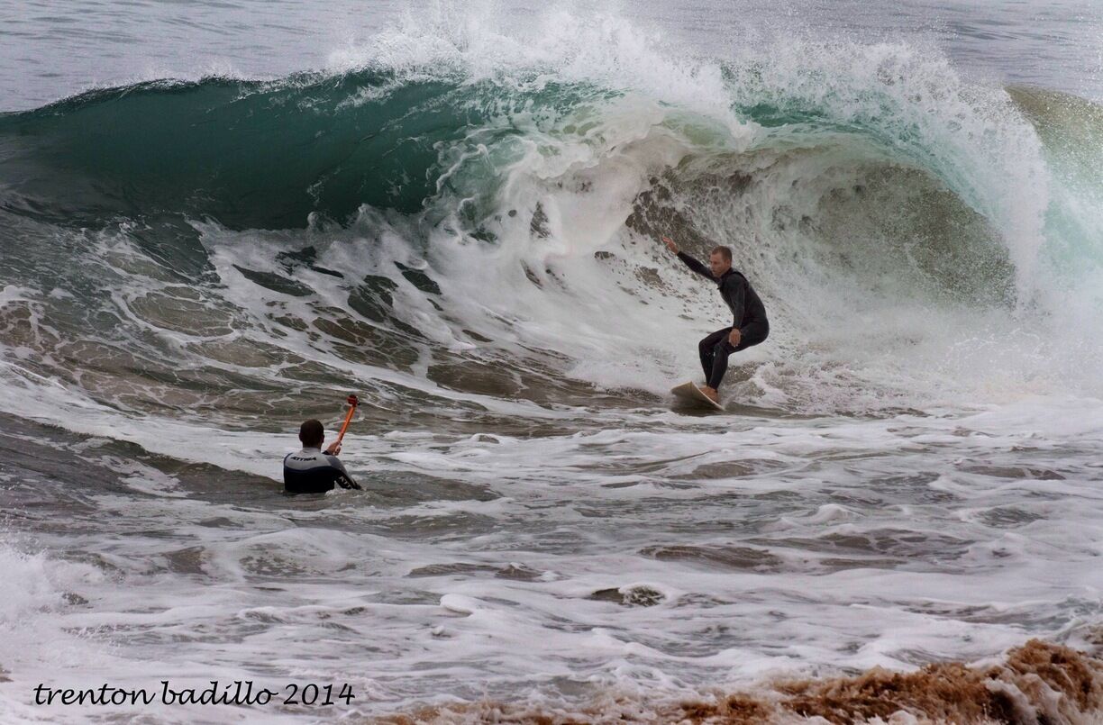 Ein Surfer reitet eine große Welle, eine andere Person beobachtet, und das Meer ist schaumig.