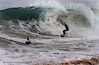 A surfer riding a large wave, another person watching, and a foamy sea.