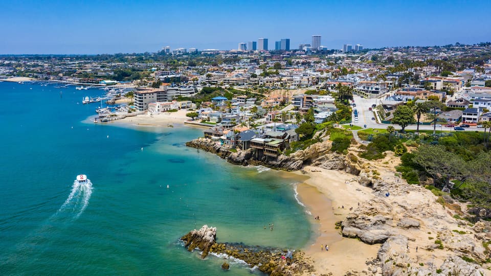 A coastal cityscape with a beach, rocky shoreline, and a marina.