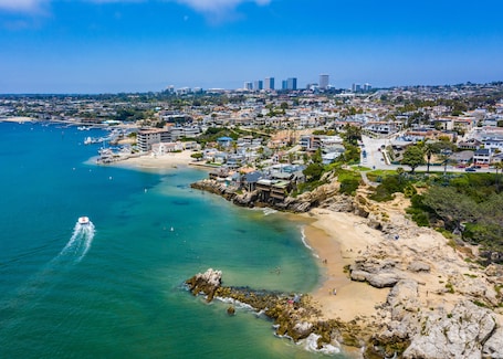 A coastal cityscape with a beach, rocky shoreline, and a marina.