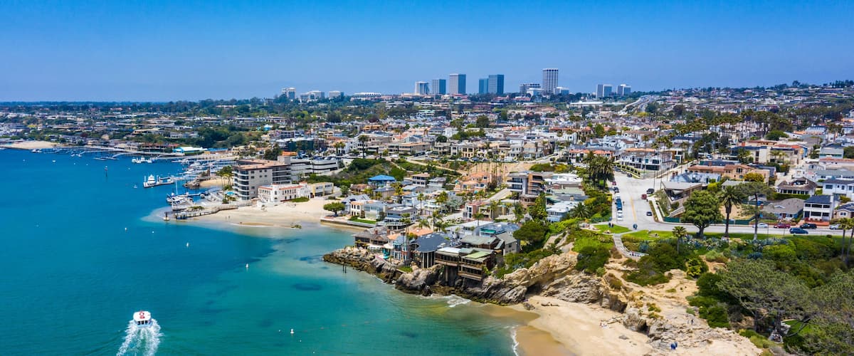 A coastal cityscape with a beach, rocky shoreline, and a marina.