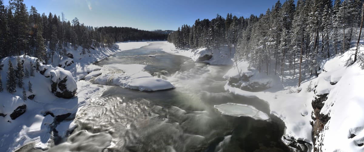 A river flowing through a snowy forest with ice formations.