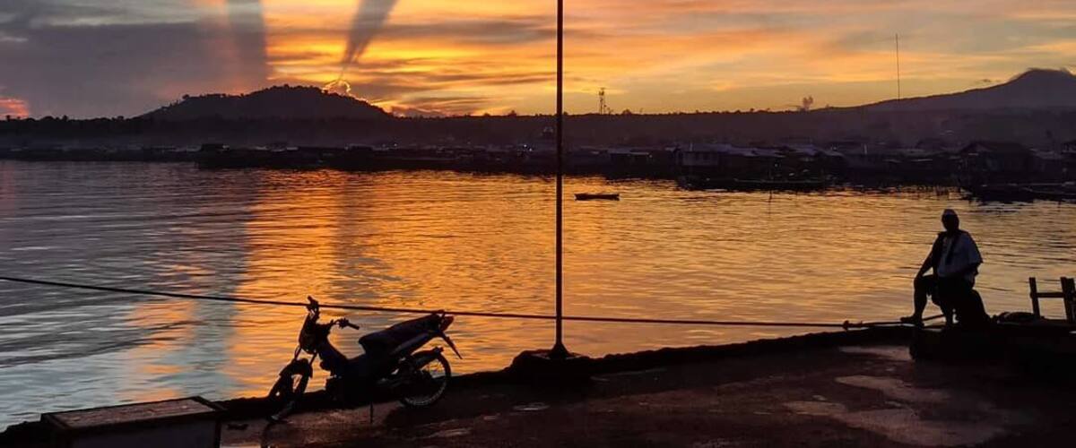 A sunset over a body of water with a silhouette of a person and a motorcycle on the shore.