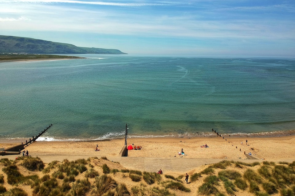 A coastal beach with dunes, a pier, and people enjoying the scenery.