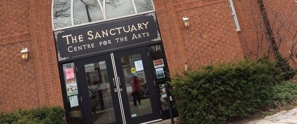 A brick building with a large arched window and a sign reading "The Sanctuary Centre for the Arts".