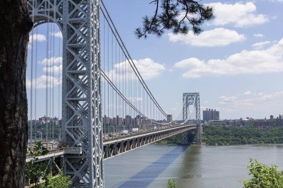 A suspension bridge over a river with a city skyline in the background.