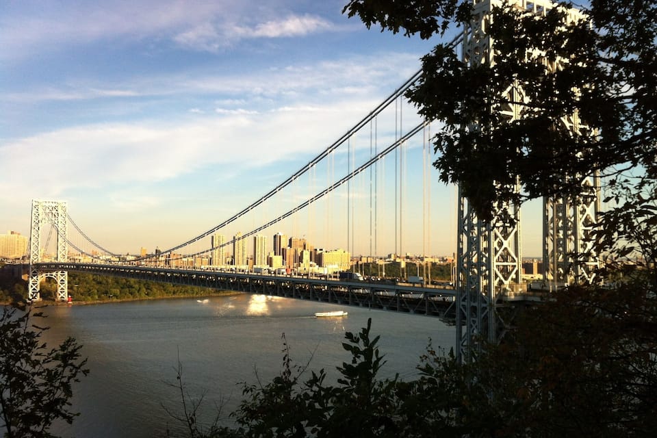 A suspension bridge over a river with city buildings in the background.