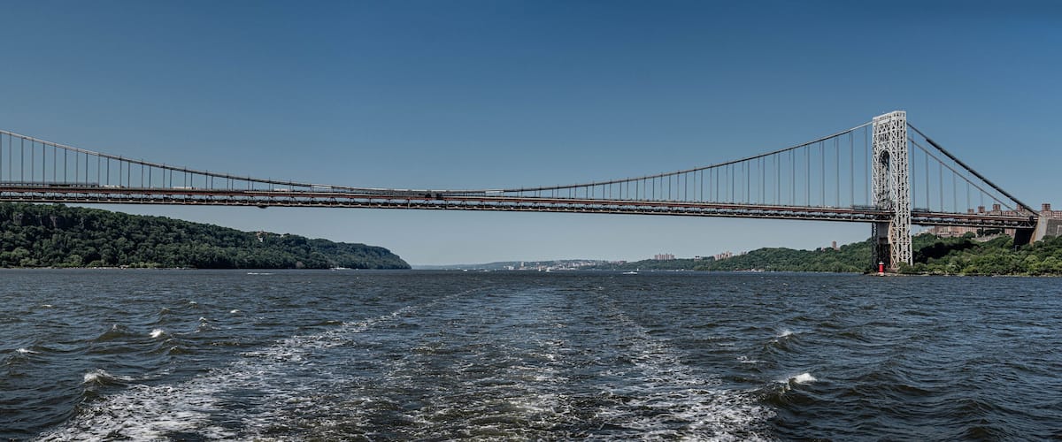 A suspension bridge over a body of water with a forested island in the background.