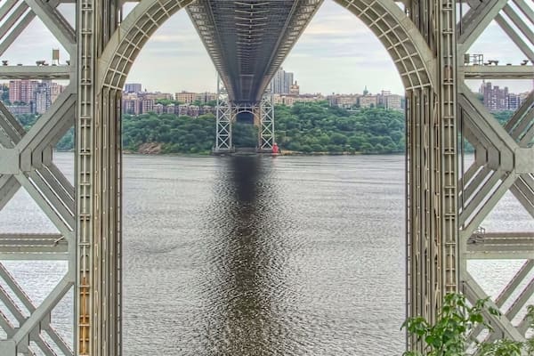 Un grand pont en acier, en forme d’arc, enjambe une rivière, avec une vue sur la ville en arrière-plan.
