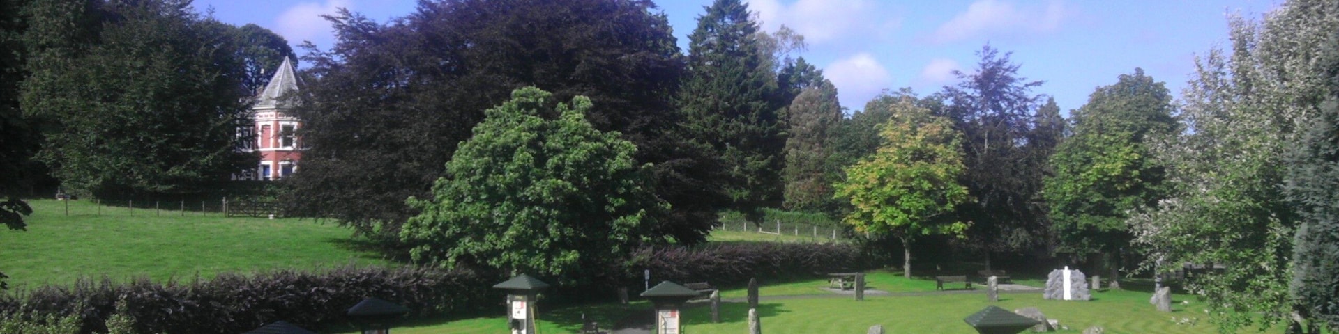 A cemetery with headstones, a gazebo, and a large tree.