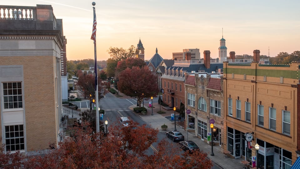 A downtown street with historic buildings, a clock tower, and autumn foliage.