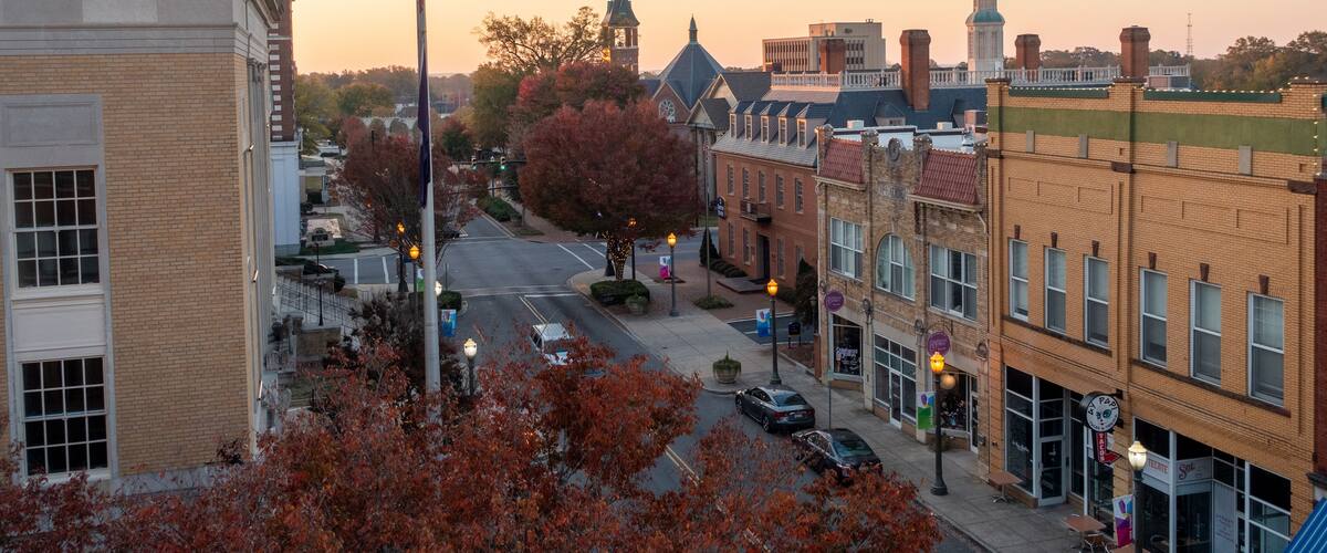 A downtown street with historic buildings, a clock tower, and autumn foliage.