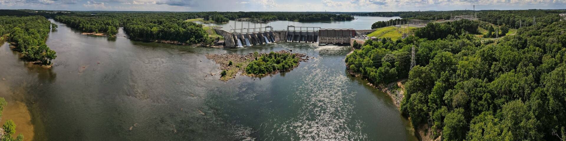 An aerial 180 degree panoramic view of a large dam and hydroelectric plant on the Catawba river in South Carolina with Lake Wylie in the background.