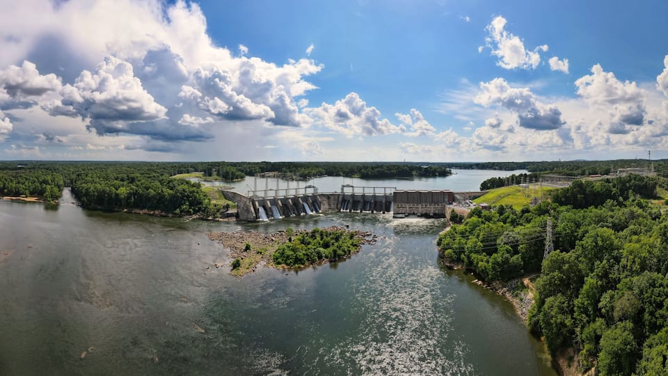 A river with a dam and waterfall, surrounded by dense greenery.