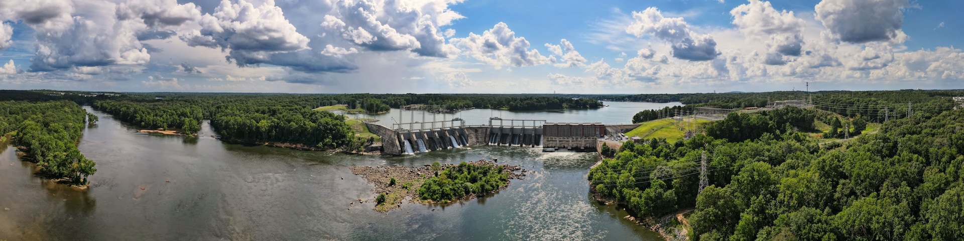An aerial 180 degree panoramic view of a large dam and hydroelectric plant on the Catawba river in South Carolina with Lake Wylie in the background.