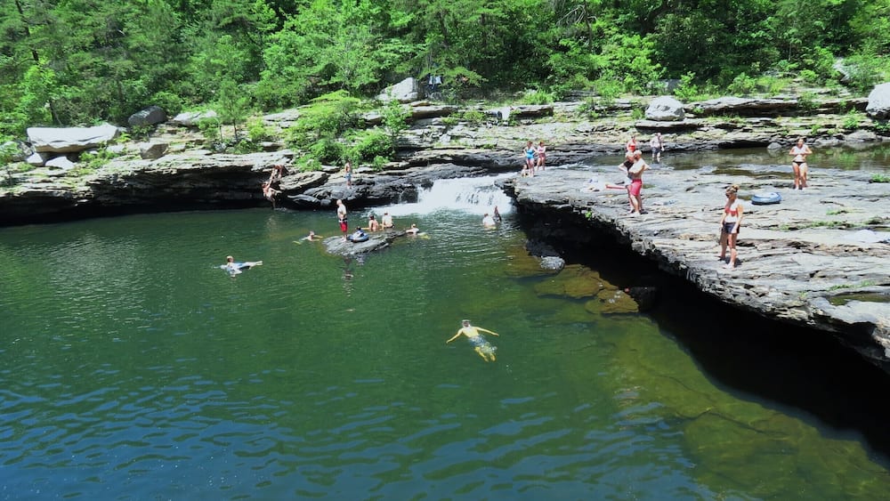 A rocky riverbank with people swimming and standing on the rocks.