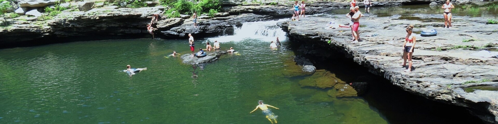 A rocky riverbank with people swimming and standing on the rocks.