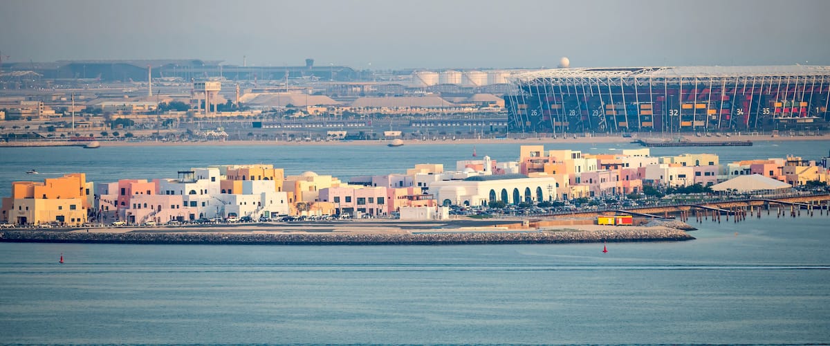 A coastal cityscape with a marina, colorful buildings, and a large industrial structure in the background.
