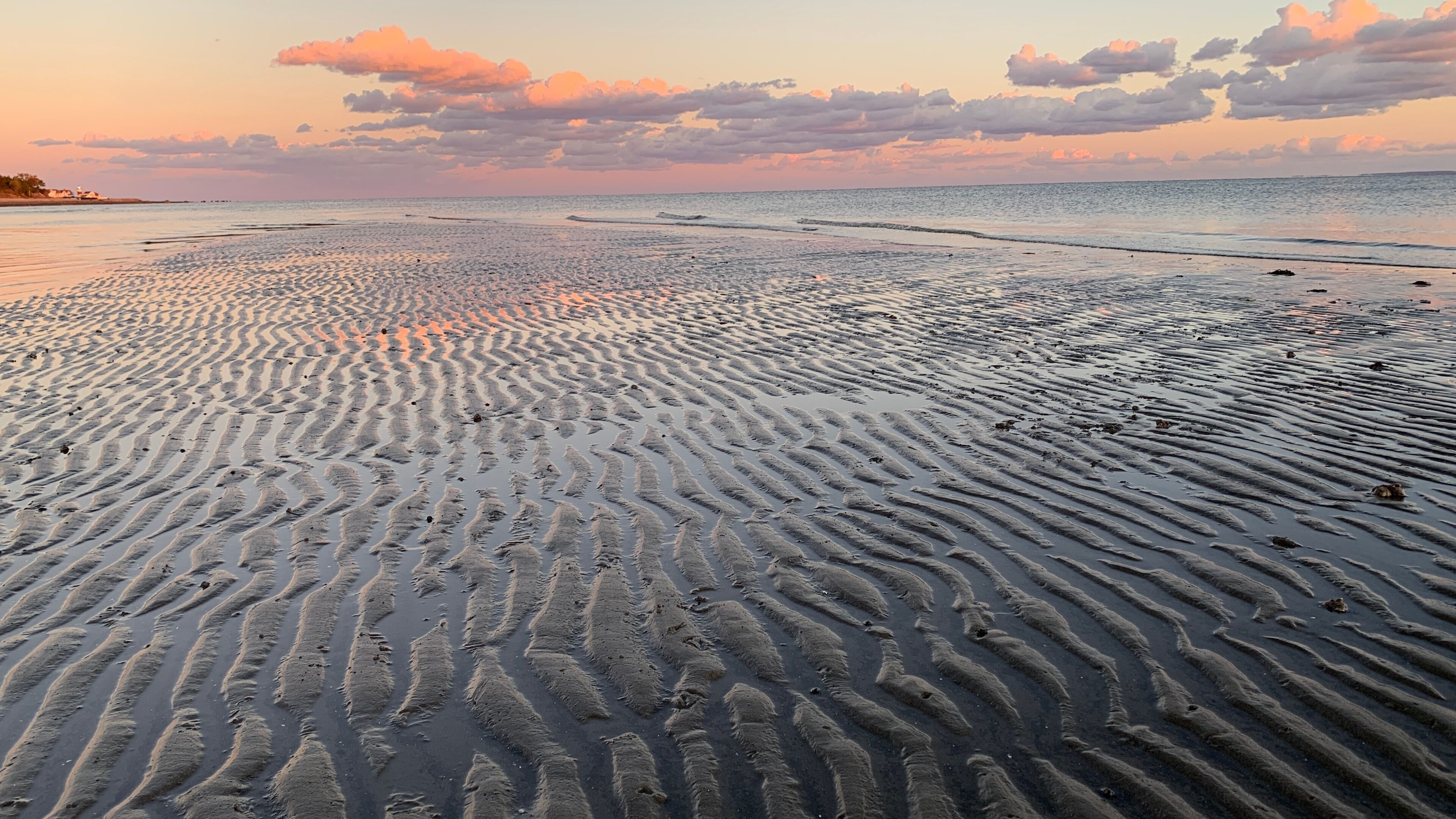 A beach with rippled sand patterns and a sunset sky.