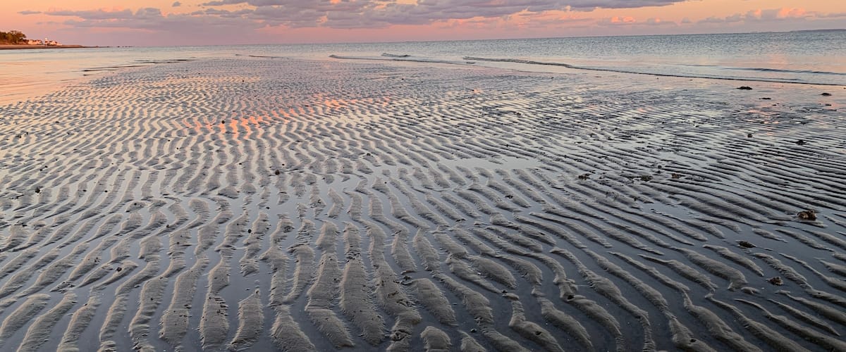 A beach with rippled sand patterns and a sunset sky.