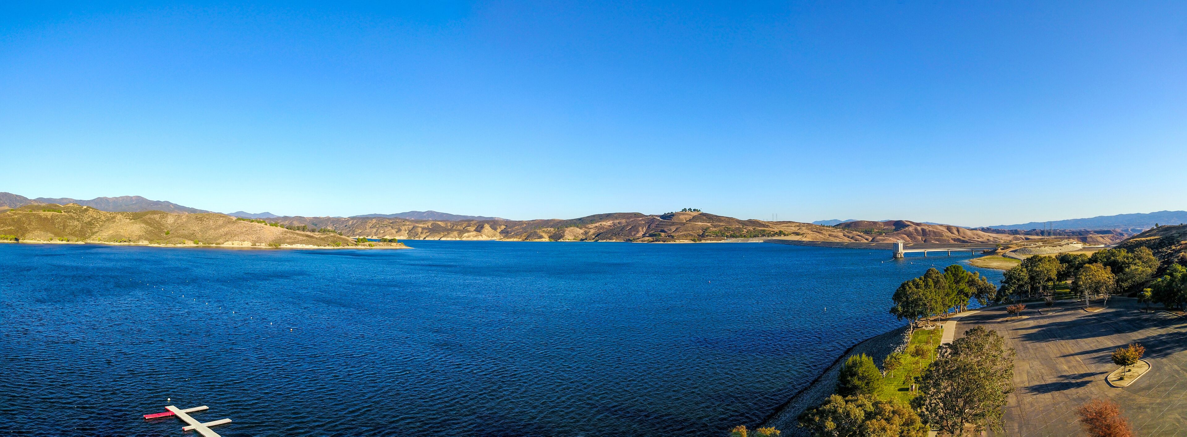 A large body of water with a bridge in the distance, surrounded by hills and trees.