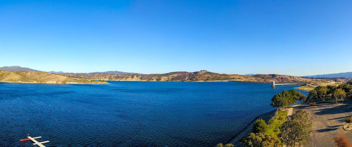 A large body of water with a bridge in the distance, surrounded by hills and trees.