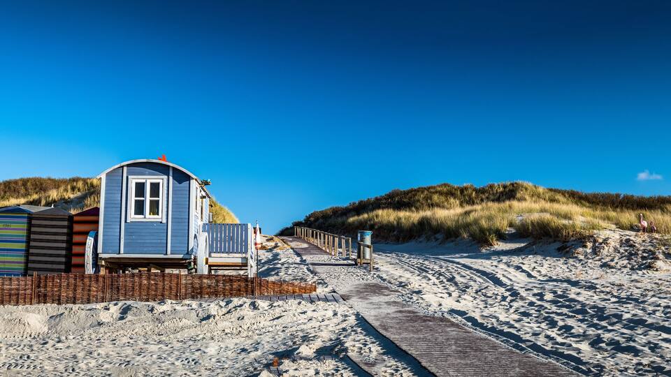 A beach with a wooden walkway, a small blue building, and colorful containers.