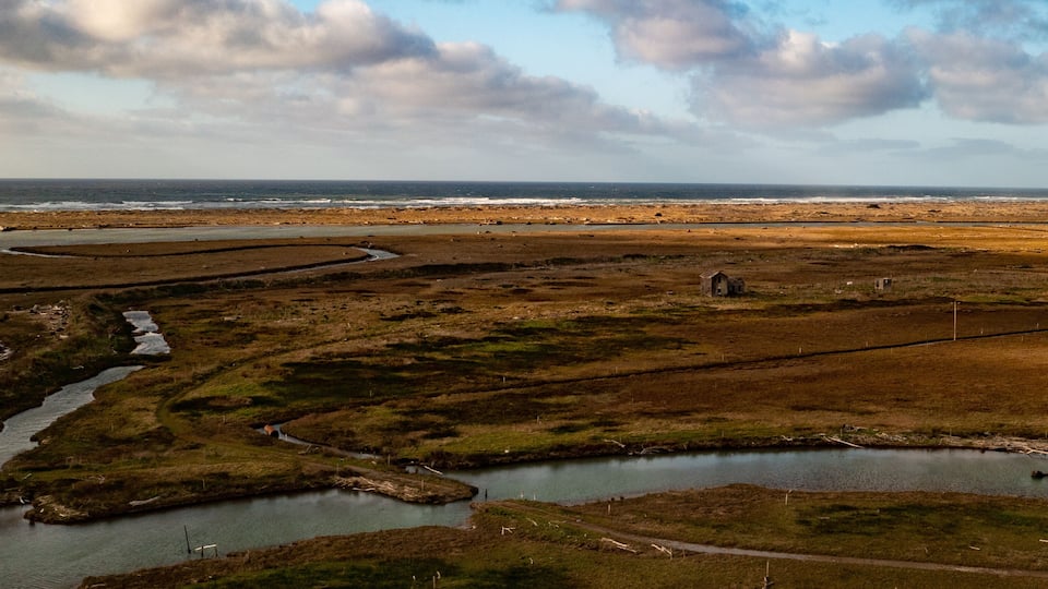 A coastal landscape with a winding river, a small pond, and a distant shoreline.