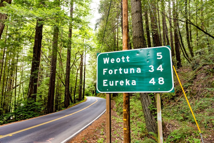 Señal de carretera en zona boscosa que indica los destinos Weott, Fortuna y Eureka, junto con las distancias.