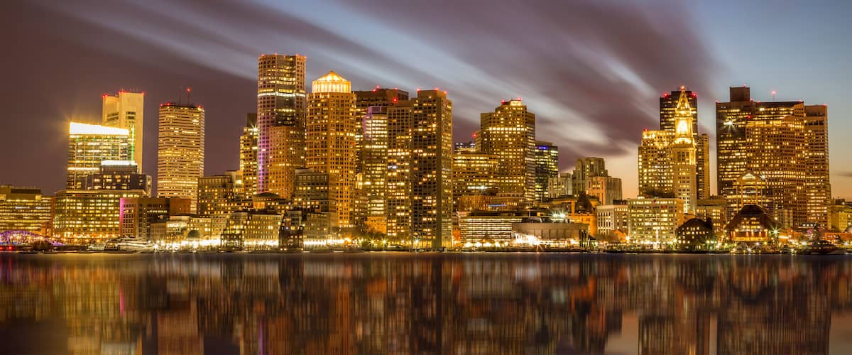 A city skyline at night with illuminated buildings reflecting on the water.