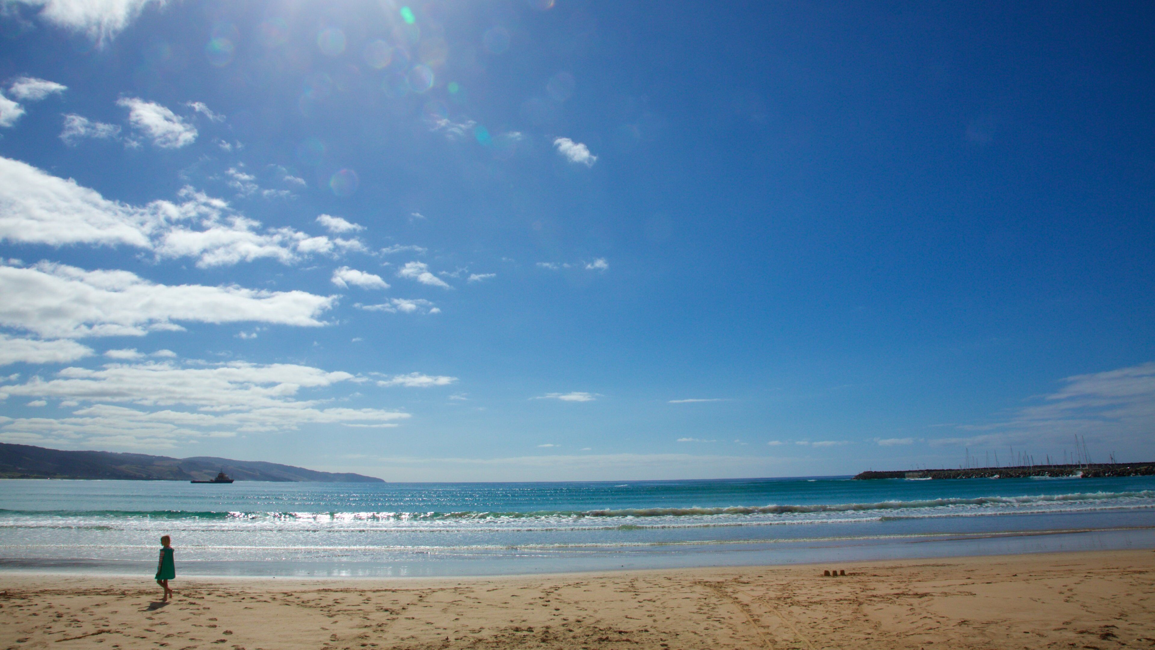 A beach with a person in a green dress, clear blue sky, and calm sea.
