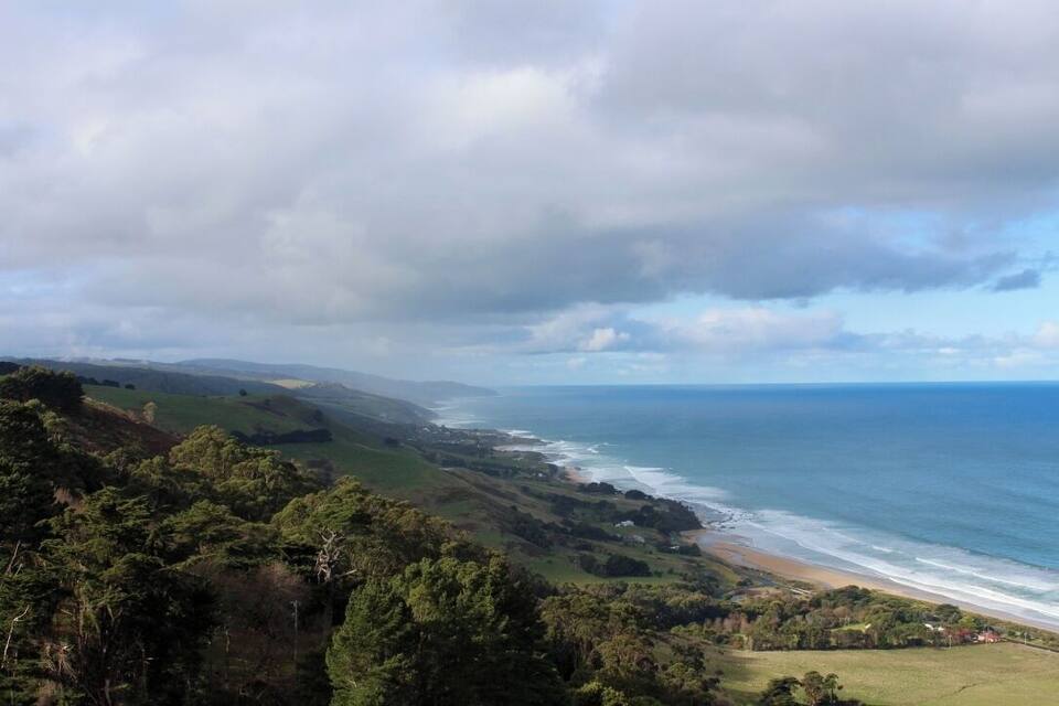 Paisaje costero con playa, colinas ondulantes y vista al océano.