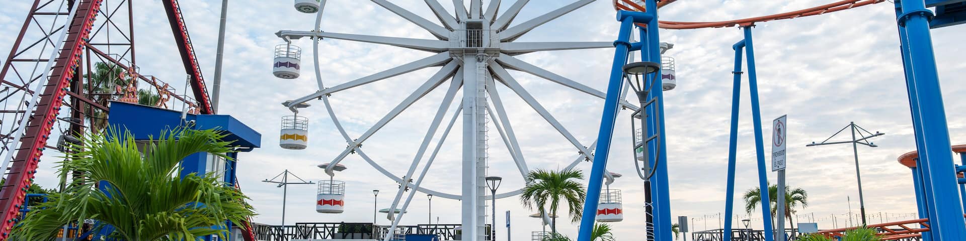 Ferris wheel and roller coasters at a closed and empty amusement park, sunny day, blue sky with white clouds. Sunset Park in La Libertad tourist beach town, El Salvador.
