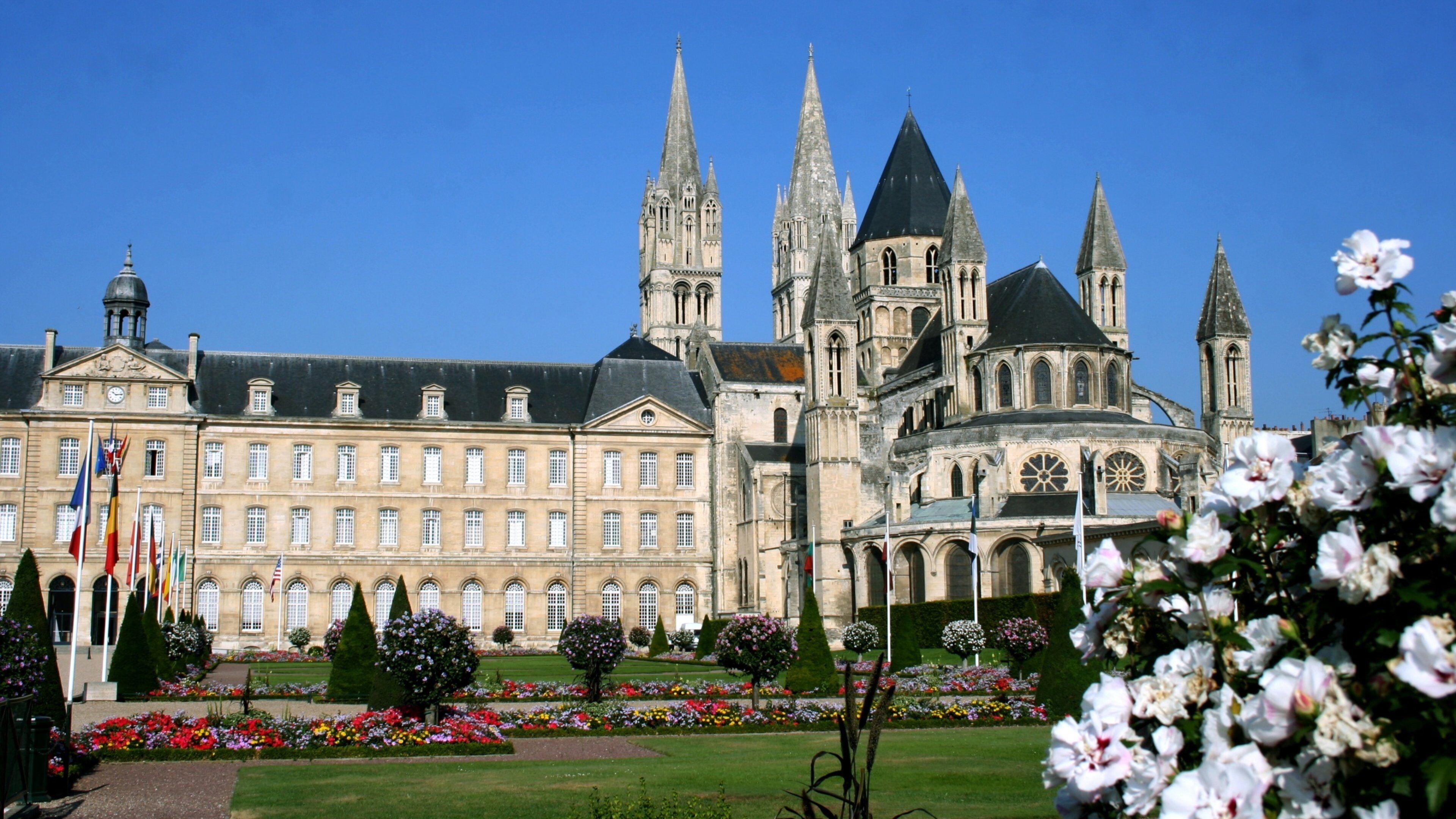 A historic building with multiple spires and a well-maintained garden with flowers.